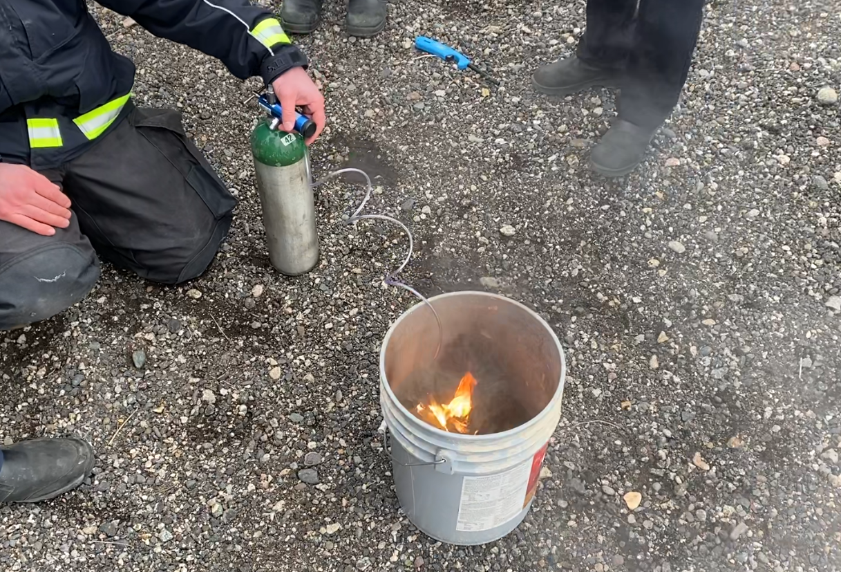 A nasal cannula fire burns inside of a bucket filled with water. 